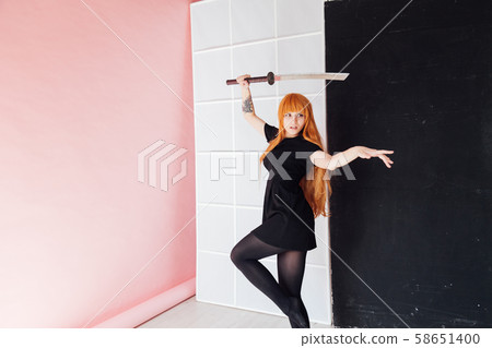 Woman cosplayer with red hair holds Japanese sword 58651400