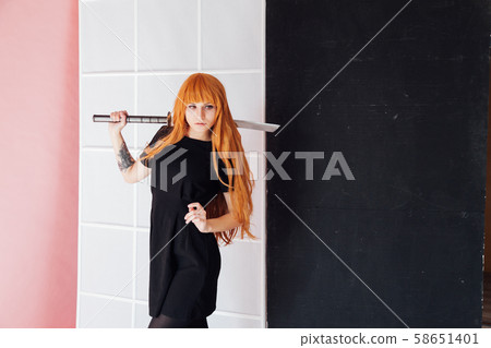 Woman cosplayer with red hair holds Japanese sword 58651401