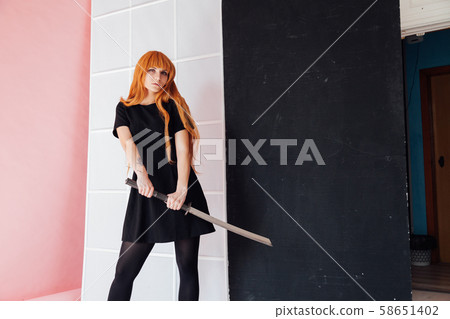 Woman cosplayer with red hair holds Japanese sword 58651402