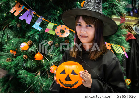 Beautiful young surprised woman or Halloween Witch dark style with holding a pumpkin and black drink in Halloween celebrate night party. Copy space background and soft or select focus 58657620