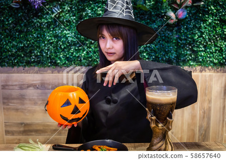 Beautiful young surprised woman or Halloween Witch dark style with holding a pumpkin and black drink in Halloween celebrate night party. Copy space background and soft or select focus 58657640