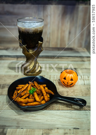 French fries in a black pan resting on a wooden table with pumpkin and cola at a Halloween party French fries in a black pan resting on a wooden table with pumpkin and cola at a Halloween party 58657985