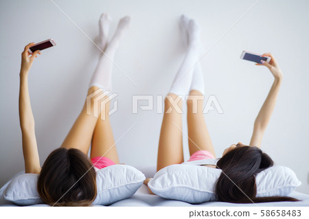 Two hot girls lying on a bed taking a photo of themselves Two hot girls lying on a bed taking a photo of themselves 58658483