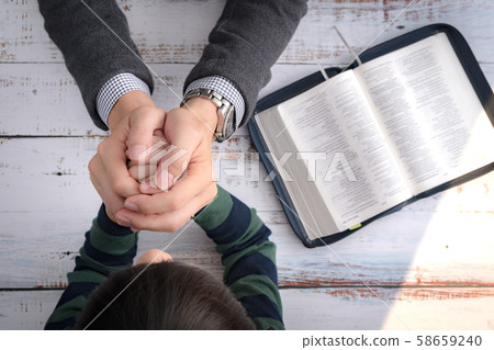 Top view closeup of a father and his little son's hands praying together after bible study in the morning. Christianity, Parenting and Raising child in God's way, Thankful moment, Happy father's day. 58659240