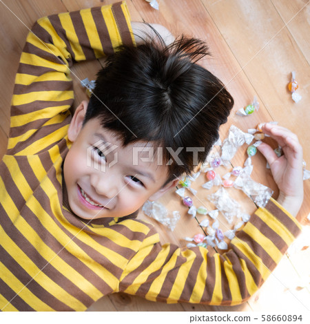 A cute little asian boy lying down among pile of sweet colorful candy, he looking at camera, smile happily showing white, strong and healthy deciduous teeth. Prevent the cavity, Cause of tooth decay. A cute little asian boy lying down among pile of sweet colorful candy, he looking at camera, smile happily showing white, strong and healthy deciduous teeth. Prevent the cavity, Cause of tooth decay. 58660894