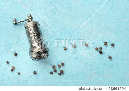 Allspice, Jamaican pepper. Black peppercorns with a vintage pepper mill, overhead shot on a blue 58661394