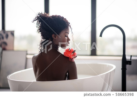 Curly dark-skinned woman holding loofah while having bath Curly dark-skinned woman holding loofah while having bath 58665398
