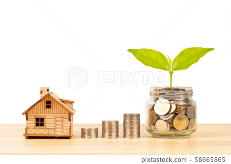 Coin jar and stack, and model house on wooden desk 58665865