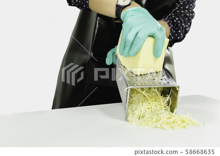Woman with green gloves grating cheese on kitchen table isolated in clipping path. 58668635