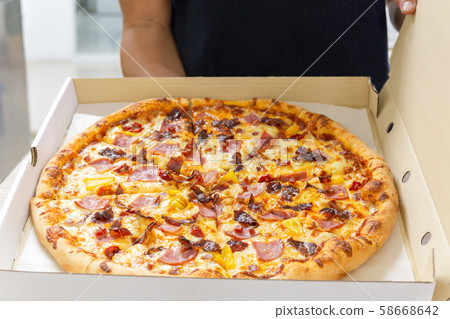 Man holds a open box of pizza in his hands and offers it to others. 58668642