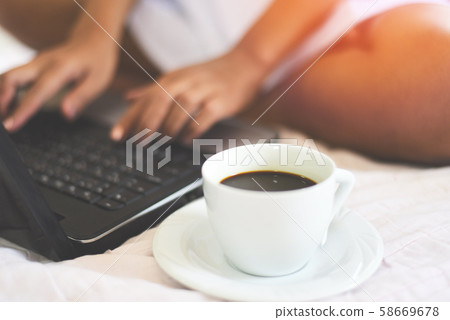 coffee cup with woman using laptop on the bed coffee cup with woman using laptop on the bed 58669678