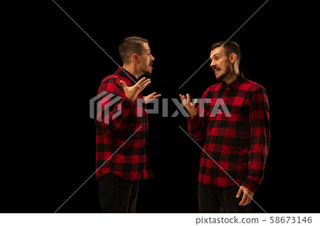 Young handsome man arguing with himself on black studio background. Young handsome man arguing with himself on black studio background. 58673146