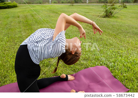 Young beautiful woman doing yoga exercise in green park. Healthy lifestyle and fitness concept. Young beautiful woman doing yoga exercise in green park. Healthy lifestyle and fitness concept. 58673442