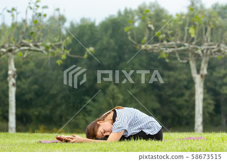 Young beautiful woman doing yoga exercise in green park. Healthy lifestyle and fitness concept. Young beautiful woman doing yoga exercise in green park. Healthy lifestyle and fitness concept. 58673515