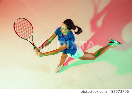 Young woman in blue shirt playing tennis in mixed light. Youth, flexibility, power and energy. Young woman in blue shirt playing tennis in mixed light. Youth, flexibility, power and energy. 58673796