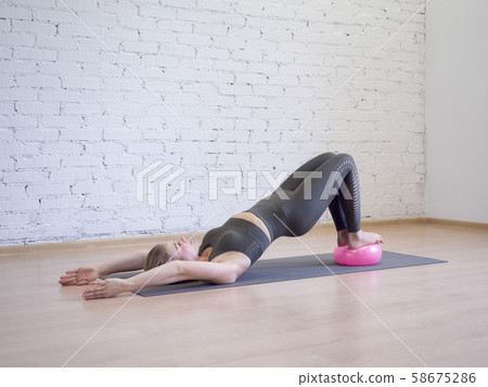 Gluteal bridge on pink small fitness ball. Young caucasian woman doing pilates with special 58675286