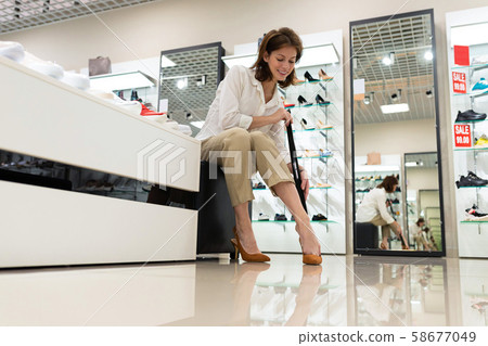 Young woman smiling and trying on heels with a help of shoehorn in shop Young woman smiling and trying on heels with a help of shoehorn in shop 58677049