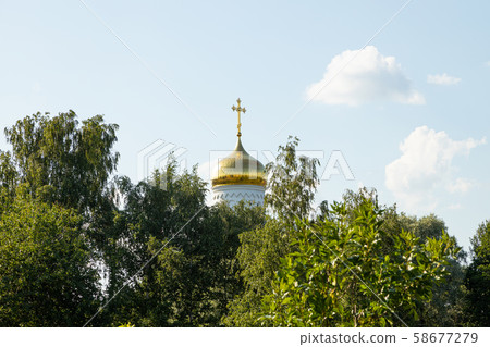 Gilt dome of white Orthodox church surrounded by green tops of trees Gilt dome of white Orthodox church surrounded by green tops of trees 58677279