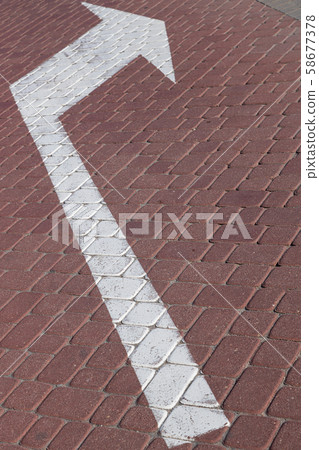 Close-up of white road marking arrow pointing to right on maroon paving flag 58677378