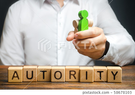 A man holds figures of people in a fist and the word Authority. High status and respect, reputation and importance. Business leader or crime boss. Submission and management control employees 58678103