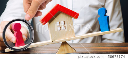 A magnifying glass looks at a female figures outweigh the balance of the scales in her favor. Separation of property and real estate after a divorce, lawyer services. trial of ownership of the house 58678174