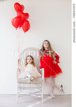 Two girls sit on a chair with red holiday balloons 58681935