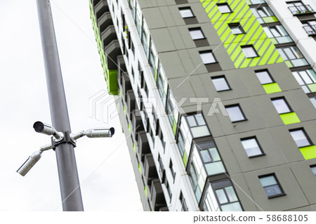 White surveillance cameras hanging on pile near high block of flats White surveillance cameras hanging on pile near high block of flats 58688105