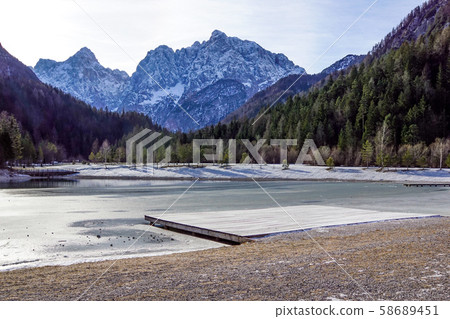 Beautiful view at sunset of the peaceful lake Fucine Tarvisio, Italy with green forest and snowy Beautiful view at sunset of the peaceful lake Fucine Tarvisio, Italy with green forest and snowy 58689451