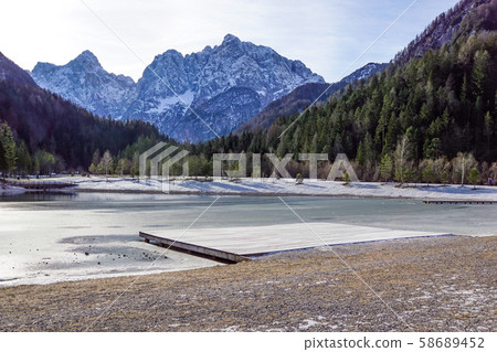 Beautiful view at sunset of the peaceful lake Fucine Tarvisio, Italy with green forest and snowy Beautiful view at sunset of the peaceful lake Fucine Tarvisio, Italy with green forest and snowy 58689452
