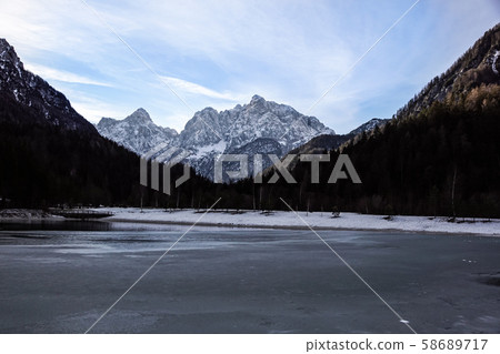 Beautiful view at sunset of the peaceful lake Fucine Tarvisio, Italy with green forest and snowy 58689717
