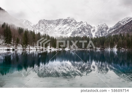 lake with green forest and snowy mountains in the background and skyfall effect. Italian lake during lake with green forest and snowy mountains in the background and skyfall effect. Italian lake during 58689754