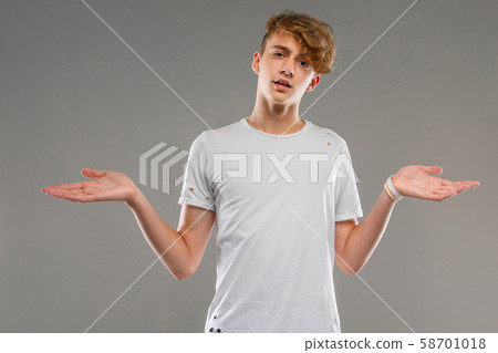 handsome emotional teenager boy posing in studio against gray, young man in a light T-shirt spreads handsome emotional teenager boy posing in studio against gray, young man in a light T-shirt spreads 58701018