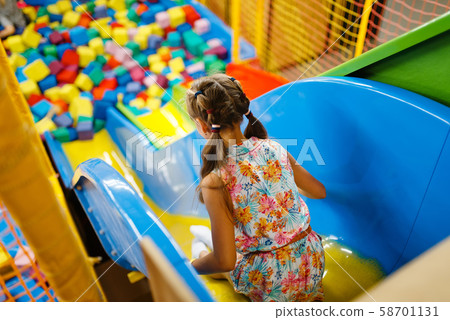 Little girl riding on plastic kids slide, playroom 58701131