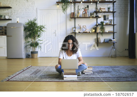 Young woman sitting and working on floor with book and laptop, business concept Young woman sitting and working on floor with book and laptop, business concept 58702657