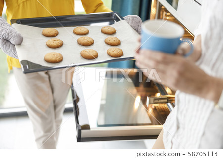 Woman is holding oven-tray in the kitchen Woman is holding oven-tray in the kitchen 58705113