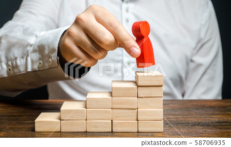 A man puts a red human figure on top of the stairs. Career growth, improvement of skills. Promotion at work of employees to leading post. The concept of success. Training. Education, business A man puts a red human figure on top of the stairs. Career growth, improvement of skills. Promotion at work of employees to leading post. The concept of success. Training. Education, business 58706935