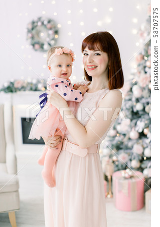 Happy family woman mother and little girl relax playing near Christmas tree on Christmas eve at home 58707575