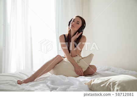 beautiful woman in laundry in the morning sits on the bed with a pillow beautiful woman in laundry in the morning sits on the bed with a pillow 58712081