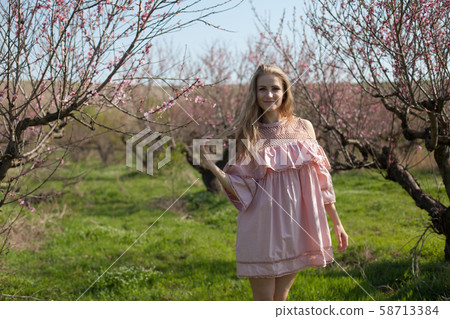 Woman blonde in pink dress walks in the flowering garden 58713384