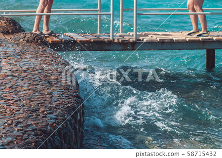 A pair of caucasian male and female feet on the wooden platform against the bright turquoise sea 58715432