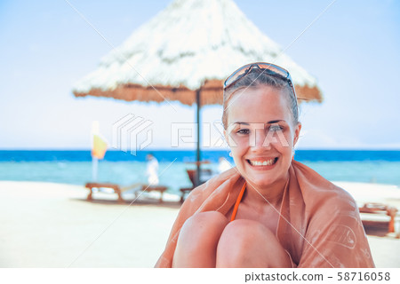 Laughing and happy girl in an orange swimsuit is sitting on the beach and enjoying the waves, behind Laughing and happy girl in an orange swimsuit is sitting on the beach and enjoying the waves, behind 58716058