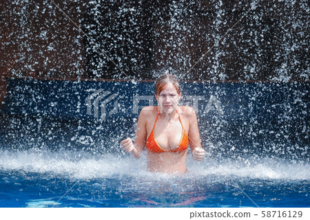 laughing and happy girl in an orange swimsuit plays jumping and having fun under a waterfall in the laughing and happy girl in an orange swimsuit plays jumping and having fun under a waterfall in the 58716129