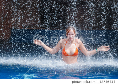 laughing and happy girl in an orange swimsuit plays jumping and having fun under a waterfall in the laughing and happy girl in an orange swimsuit plays jumping and having fun under a waterfall in the 58716131