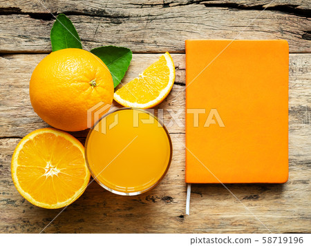a glass of fresh orange juice and group of fresh orange fruits with green leaves, on wooden background with orange cover book color. vitamin C and fruit product display or montage, studio shot 58719196