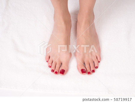 Female slim bare feet on white terry towel, close up. Red classic pedicure 58719917