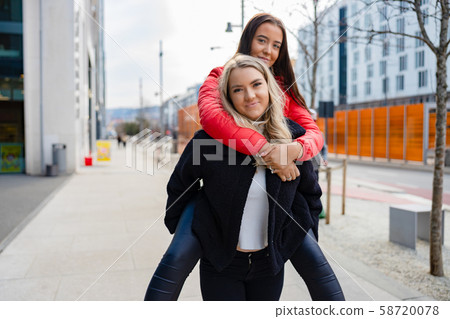 Smiling Female Friends Having Fun and Piggybacking In City Environment 58720078