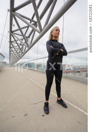 Confident Woman in Black Workout Wear Standing At Modern Bridge In City Confident Woman in Black Workout Wear Standing At Modern Bridge In City 58722081