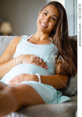 Positive pregnant woman in dress on the sofa holding on belly Positive pregnant woman in dress on the sofa holding on belly 58723878