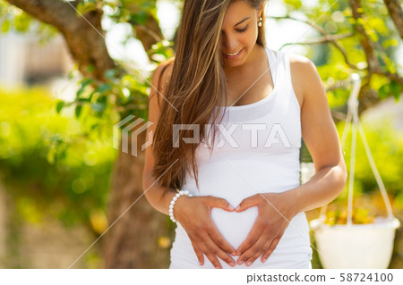 Smiling pregnant woman outdoor forming a heart on the belly 58724100