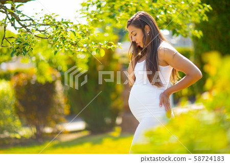 Pregnant woman in beautiful garden looking down at her belly 58724183